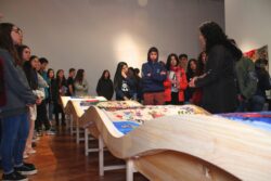 Bordar el Desborde La curadora Andrea Durán realiza una visita guiada con público joven frente a las mesas curvas de la exposición en el MNBA