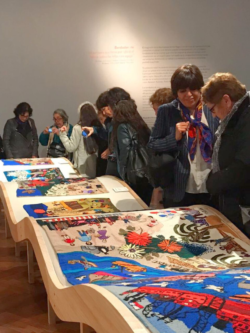 Bordar el Desborde Público y bordadoras frente a mesas curvas con obras de la colección de la Isla Negra Foundation en la inauguración de la exposición en el Bellas Artes