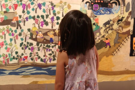 The Collective Embroidery Una niña frente a la obra Bordado Colectivo, destacando la escala de la pieza y su impacto en nuevas generaciones